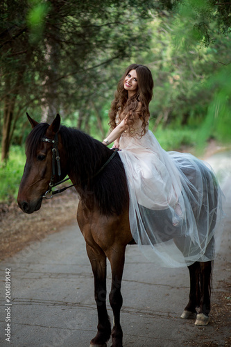 beautiful girl in a smart dress sits on horseback and smiles on nature background © Shkriabii