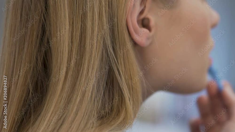 Blond girl applying lipgloss, concept of natural beauty, soft face skin closeup Blond girl applying lipgloss, concept of natural beauty, soft face skin closeup