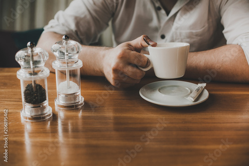 closeup of man s hands hold a cup of coffee on a wooden table with salt and pepper