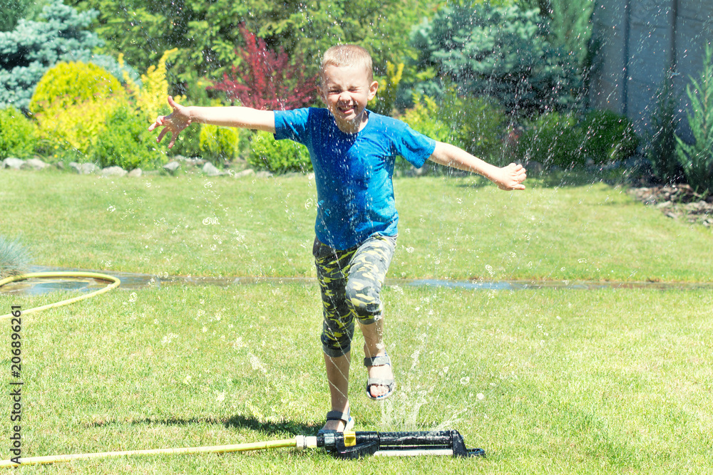 Fototapeta premium Boy running on the lawn sprinkler playing with water splashes . Summer vacation day.