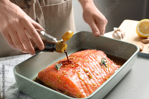 Fotografi Woman pouring marinade onto raw salmon in baking dish, closeup