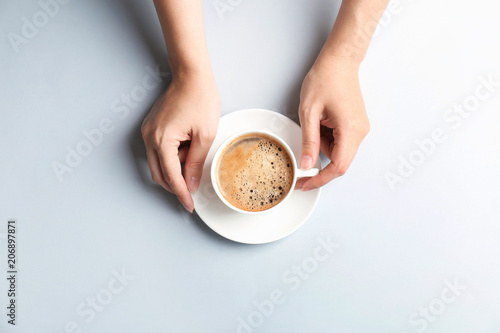 Young woman with cup of delicious hot coffee on light background, top view