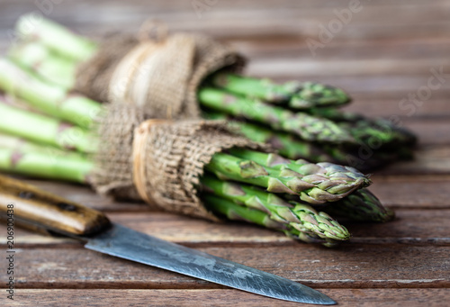 Wrapped asparagus in jute on wooden background and knife in the front.