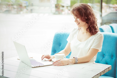 Smiling young attractive business woman sitting in a cafe with a laptop and coffee