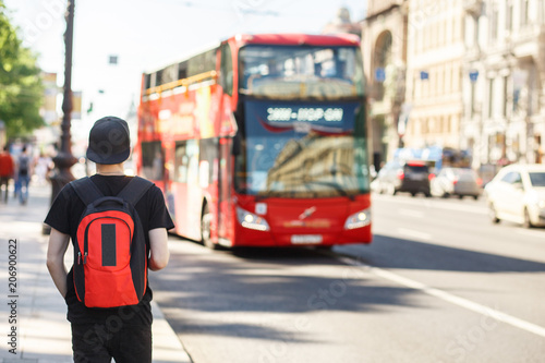 People, travel, tourism and education concept - stylish young man with backpack over london city bus on street background