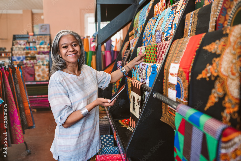 Smiling mature woman looking at colorful fabric in her shop Smiling mature woman looking at colorful fabric in her shop