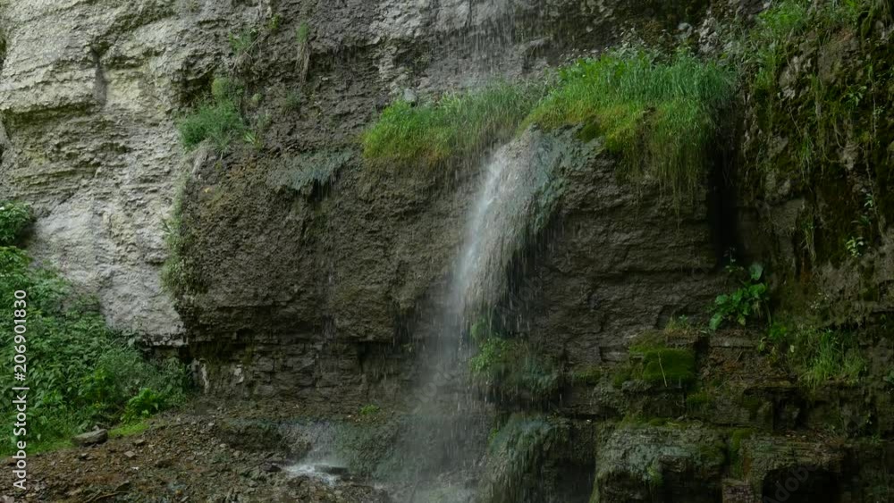 shot backing up from a long thin waterfall as it pours down the side of a rocky and mossy cliff shot backing up from a long thin waterfall as it pours down the side of a rocky and mossy cliff