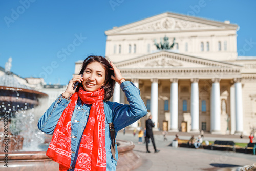 Happy cheerful traveler girl talking by phone at the Bolshoi Theatre in the background