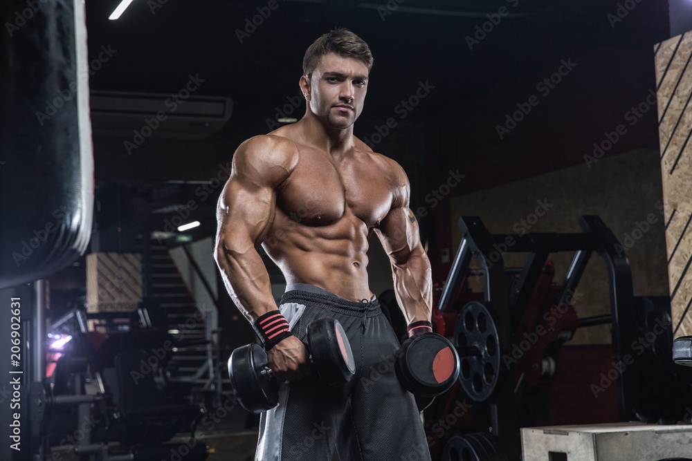 Handsome young fit muscular caucasian man of model appearance workout training in the gym gaining weight pumping up muscle and poses fitness and bodybuilding sport nutrition concept