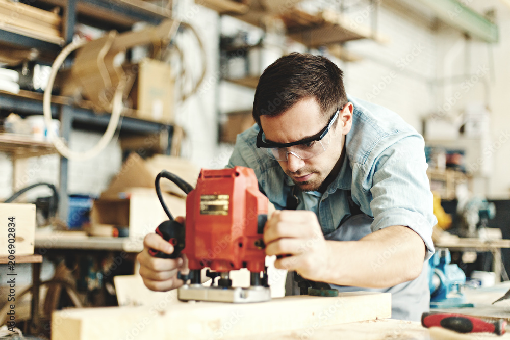 Professional carpenter concentrated on wood sanding. Young man wearing protective eyeglasses and using sanding machine
