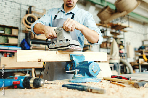 Hands of skillful young carpenter sanding wood plank placed in workbench vice