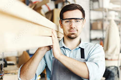 Obraz na plátně Portrait of professional young carpenter carrying wood planks on his shoulder