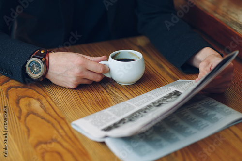  Man's hands close-up holding cup of coffee and a newspaper