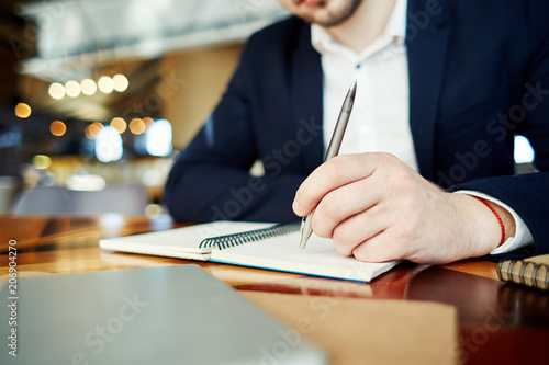 Unrecognizable businessman holding pen in his hand and thinking over notes in his notebook