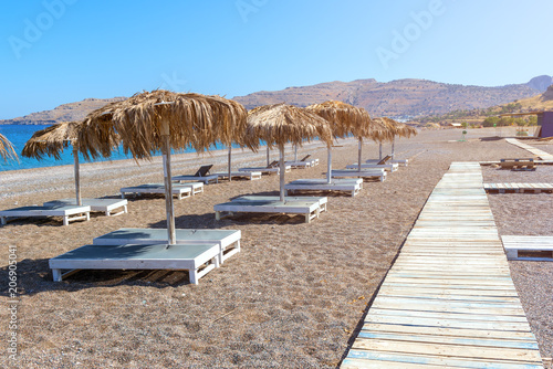 Wooden walkway and sun loungers with umbrellas on beautiful Kalathos beach. Rhodes island  GreeceWooden walkway and sun loungers with umbrellas on beautiful Kalathos beach. Rhodes island  Greece