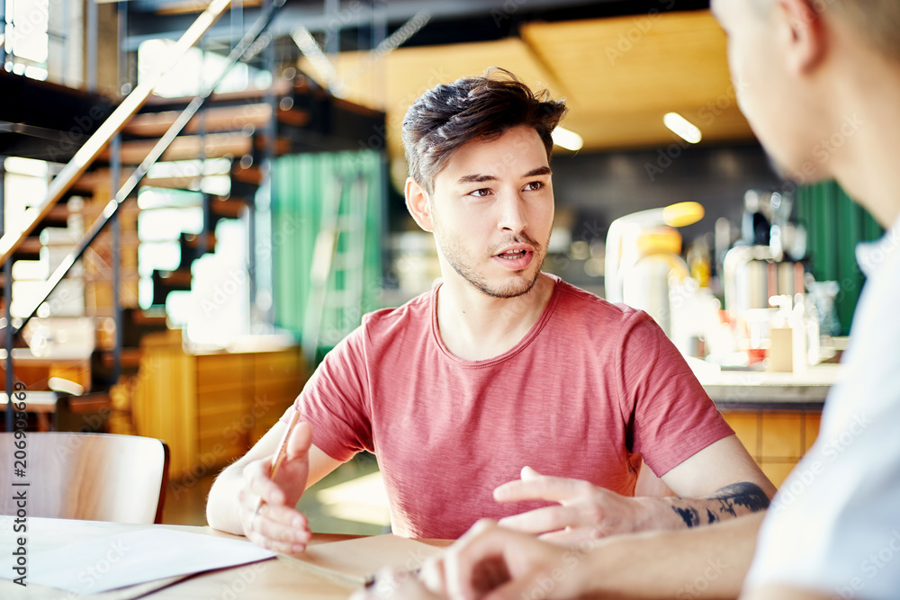 Young Hispanic man explaining his idea to colleague while sitting at table in cafe