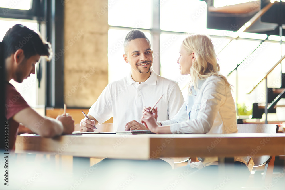 Team of young business people in casual clothes sitting at table in cafeteria and brainstorming Team of young business people in casual clothes sitting at table in cafeteria and brainstorming
