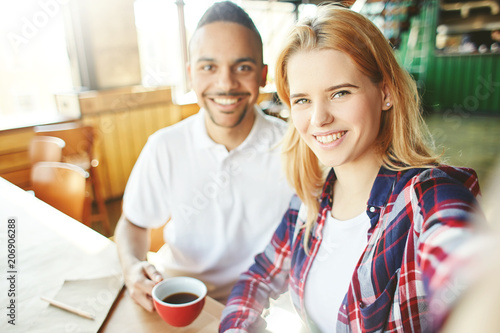 Friendly fellow stundets or young coworkers, Caucasian woman and Latin American man, taking selfie together at coffee break