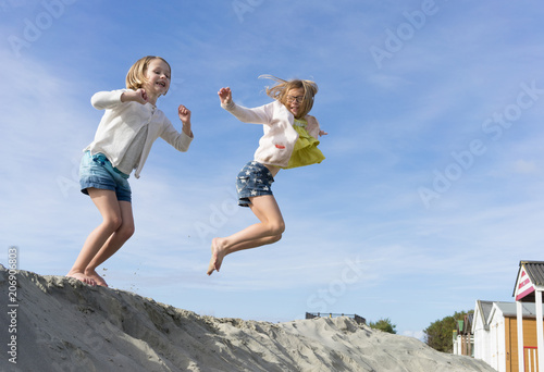 Two girls jumping off a sand hill