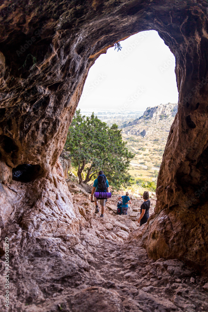 Three tourists resting cave entrance looking at landscape.