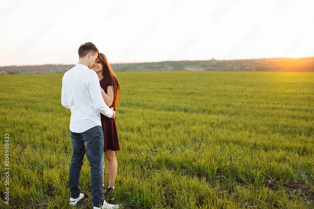 young, happy, loving couple, at sunset, standing in a green field, against the sky, in the arms, and enjoying each other, advertising and inserting text