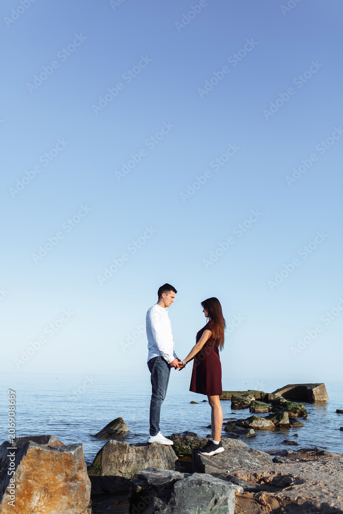 young, happy, loving couple standing on the rocks at sea, in the arms, and looking at each other, advertising and inserting text young, happy, loving couple standing on the rocks at sea, in the arms, and looking at each other, advertising and inserting text