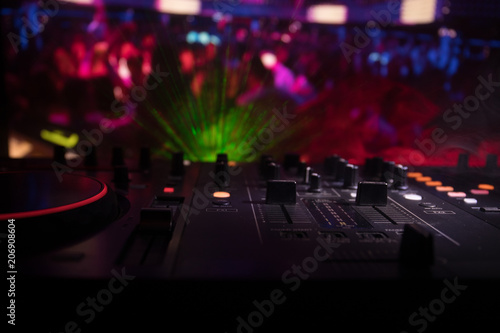 In selective focus of Pro dj controller.The DJ console deejay mixing desk at music party in nightclub with colored disco lights.