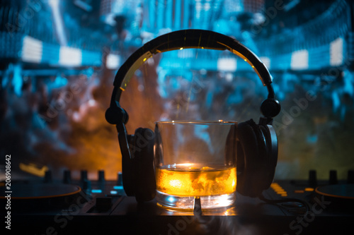 Glass with whisky with ice cube inside on dj controller at nightclub. Dj Console with club drink at music party in nightclub with disco lights.