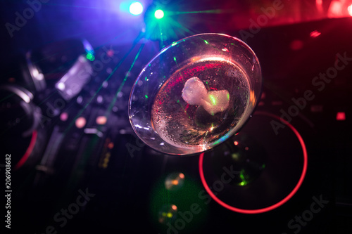 Glass with martini with olive inside on dj controller in night club. Dj Console with club drink at music party in nightclub with disco lights. Close up view
