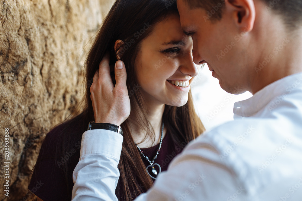 young, happy, loving couple, near the sand wall, on the sea, in the arms, and look at each other, advertising and inserting text young, happy, loving couple, near the sand wall, on the sea, in the arms, and look at each other, advertising and inserting text