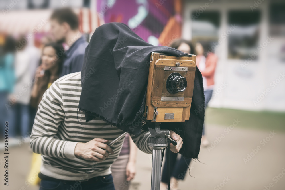Photographer with antiquity vintage wooden camera under dark cloth cape photographing passers - old classical action, rarity concept