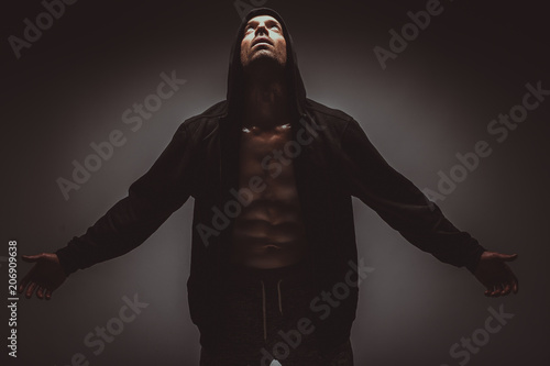 Strong young man with muscular body in black sport jacket with hood. Horizontal picture