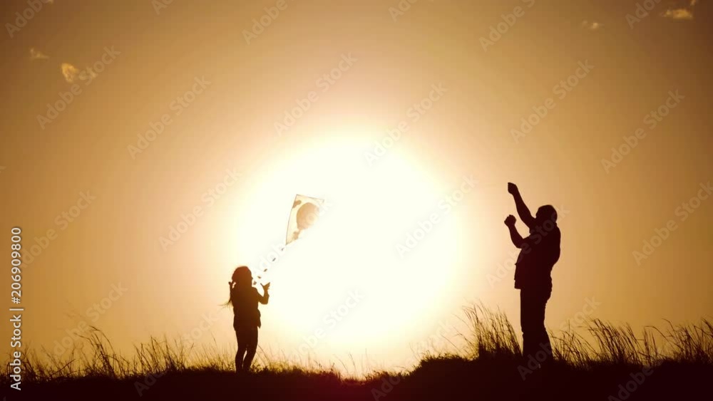 Silhouette of a happy family playing a kite. Grandpa and little girl are playing at sunset with a kite. Silhouette of a happy family playing a kite. Grandpa and little girl are playing at sunset with a kite.