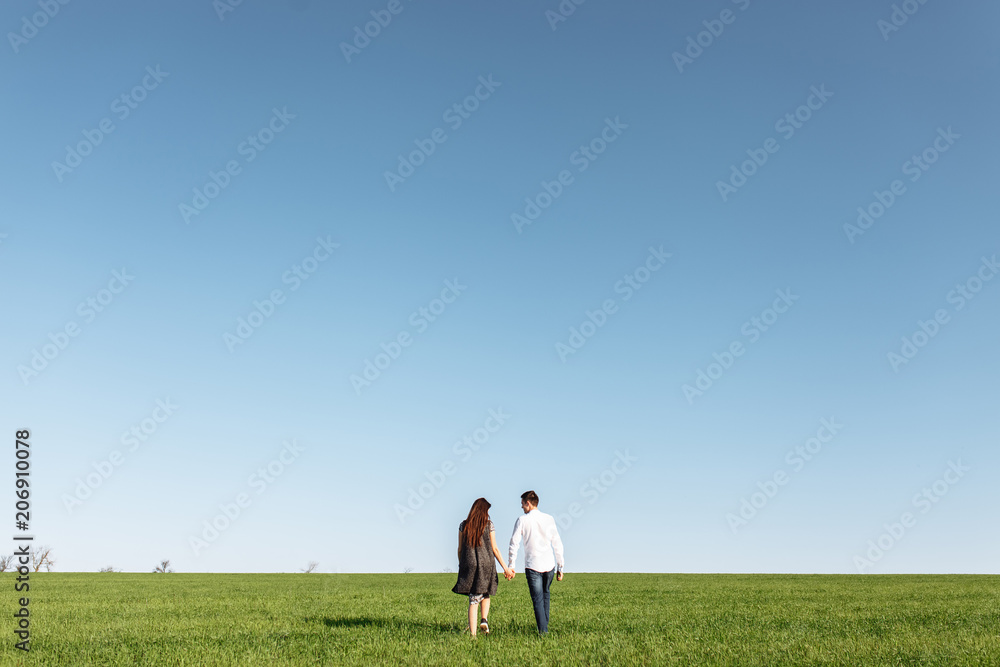 a young, happy, loving couple, standing in a green field, against the sky by the hands , and enjoy each other, advertising, and inserting text a young, happy, loving couple, standing in a green field, against the sky by the hands , and enjoy each other, advertising, and inserting text