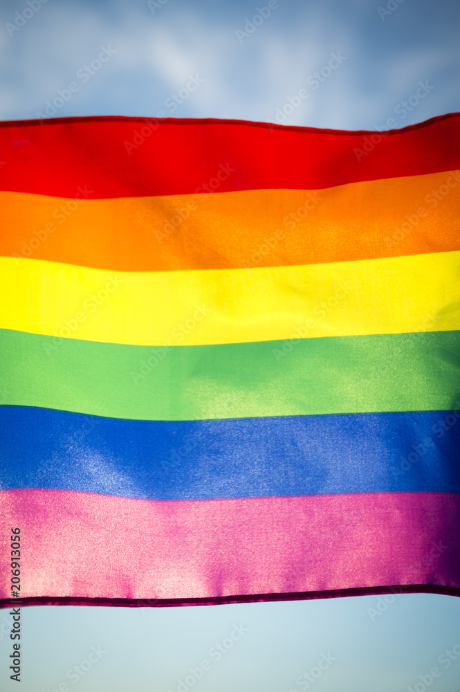 Fototapeta premium Rainbow flag flying in bright sun on the sidelines of a colorful summer gay pride parade