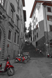 Artistic black and white photo of a narrow street with red motorbikes and steps at background. Selective color effect. Florence, Italy.