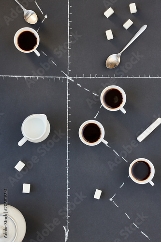 Above view of coffee cups and sugar cubes laid over grey background with chalk graph on it , business, statistics, development or deadline concept, copy space