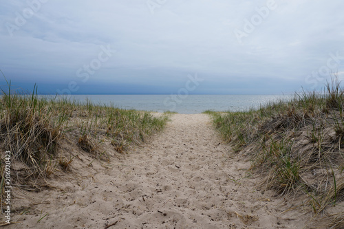 Fototapeta Naklejka Na Ścianę i Meble -  Sand with beach grass in foreground, cloudy sky, lake in background