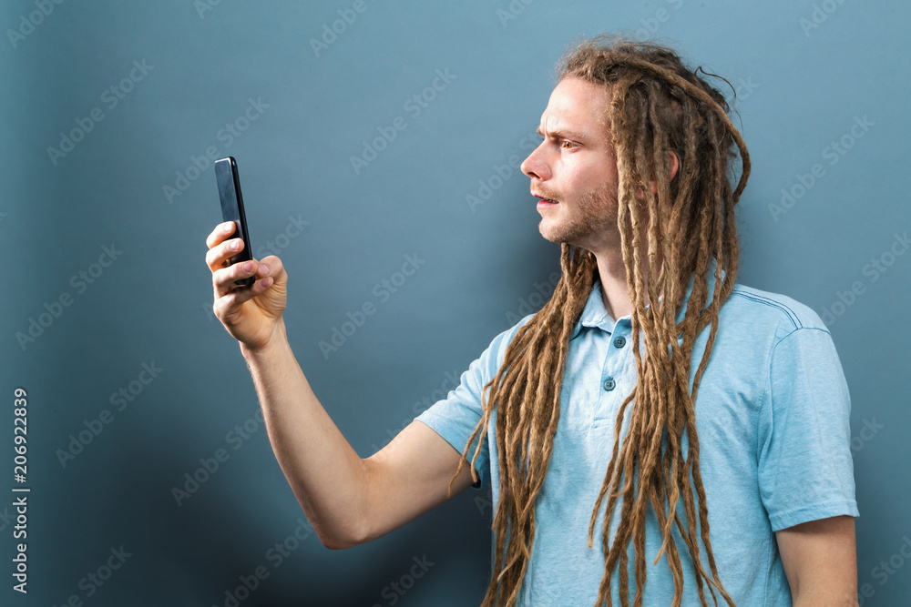 Young man staring at his cellphone on a gray background Young man staring at his cellphone on a gray background