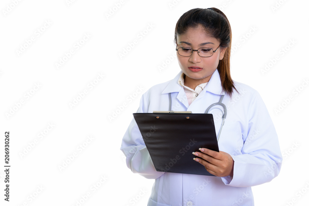 Studio shot of young fat Persian woman doctor reading on clipboa Studio shot of young fat Persian woman doctor reading on clipboa