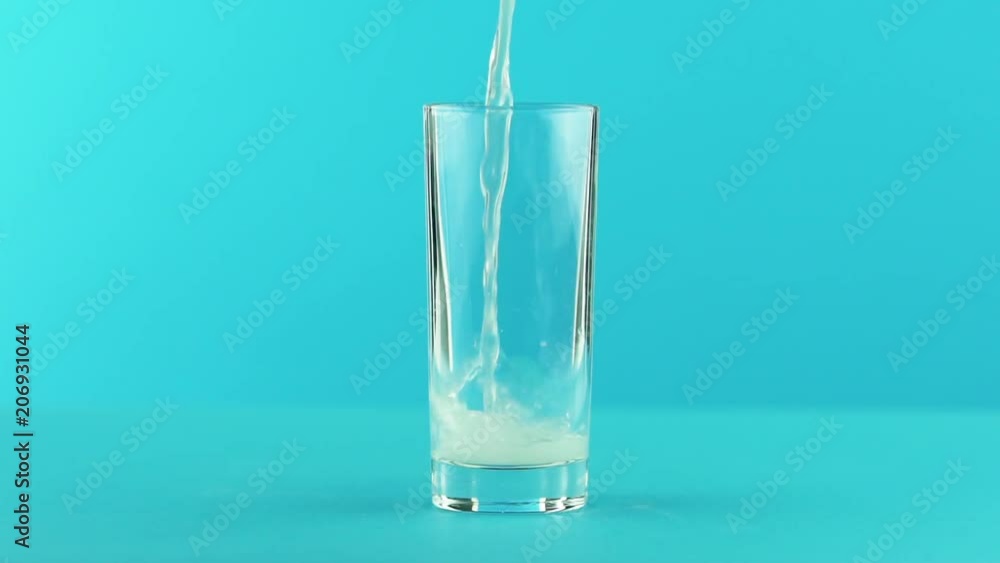 Slow motion close-up shot of fruit fizzy lemonade soda cold beverage drink pooring into glass blue background in studio Slow motion close-up shot of fruit fizzy lemonade soda cold beverage drink pooring into glass blue background in studio