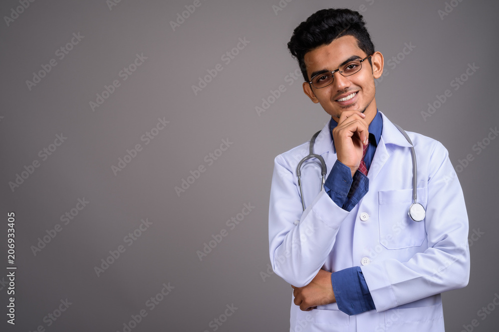 Young Indian man doctor against gray background