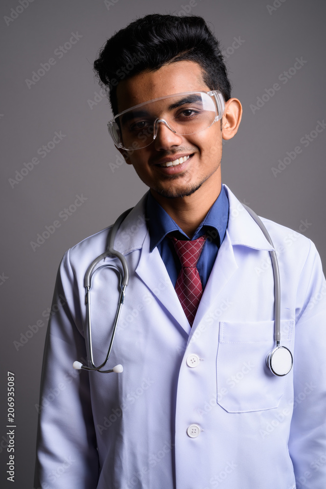 Young Indian man doctor wearing protective glasses against gray 