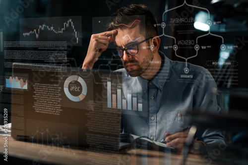Man in eyeglasses watching monitor of computer sitting alone late at night in office having overhours.