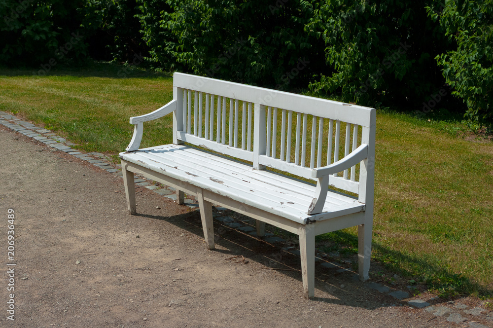 White bench made of wood. The bench is located in some park.