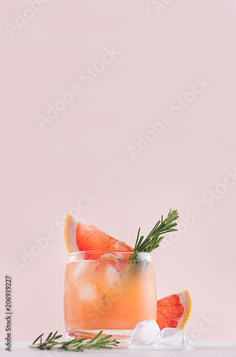 Summer fresh homemade grapefruit lemonade with ice cubes and rosemary closeup on light pink background, vertical.