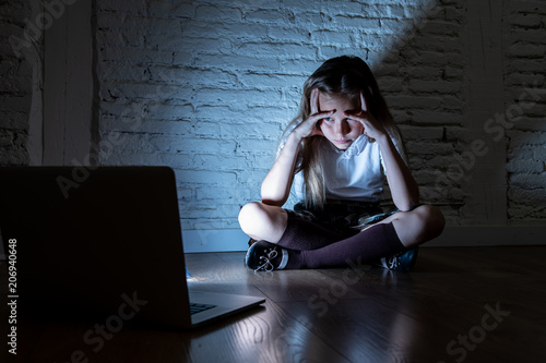 Sad young girl with laptop suffering bullying and harassment online. Cyberbullying, online gaming photo