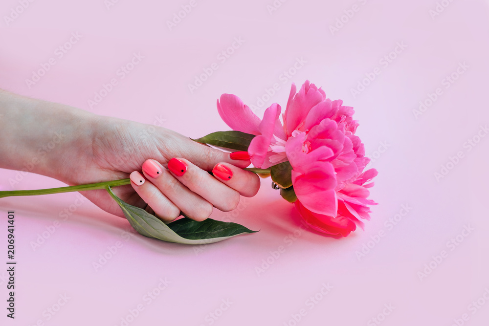 Creative bright trendy summer manicure with nails of different color. Female hand with art nail design on pink background and fuchsia peony flower.