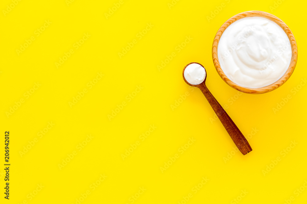 Healthy product, healthy meal. Greek yogurt in brown bowl near spoon on yellow background top view copy space Healthy product, healthy meal. Greek yogurt in brown bowl near spoon on yellow background top view copy space