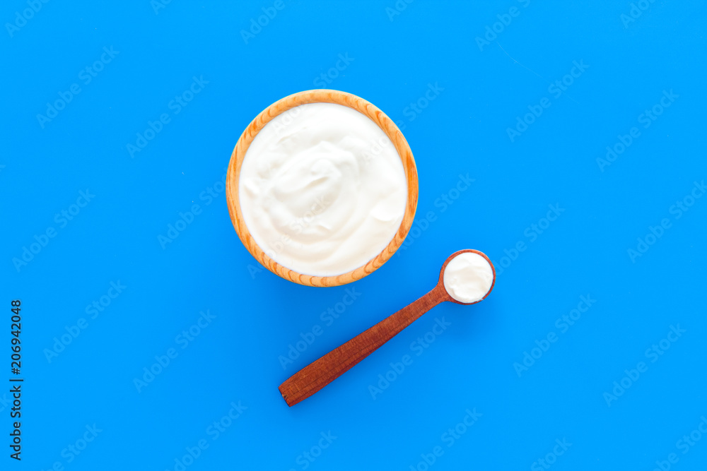 Healthy product, healthy meal. Greek yogurt in brown bowl near spoon on blue background top view copy space Healthy product, healthy meal. Greek yogurt in brown bowl near spoon on blue background top view copy space